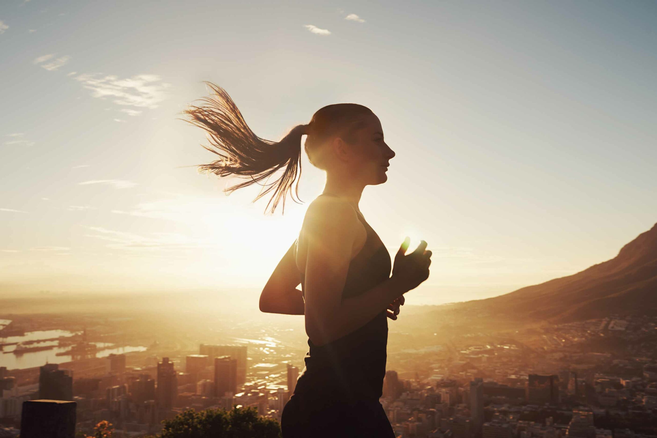 A woman runs at sunset with the view of a city in the background.