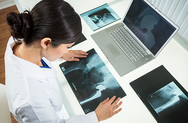 A doctor reviews a set of X-rays while sitting at a desk.